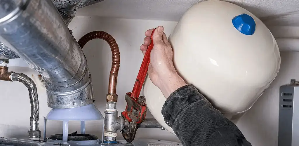 Water heater repair technician tightening plumbing connections near a tank unit in Evansville, IN